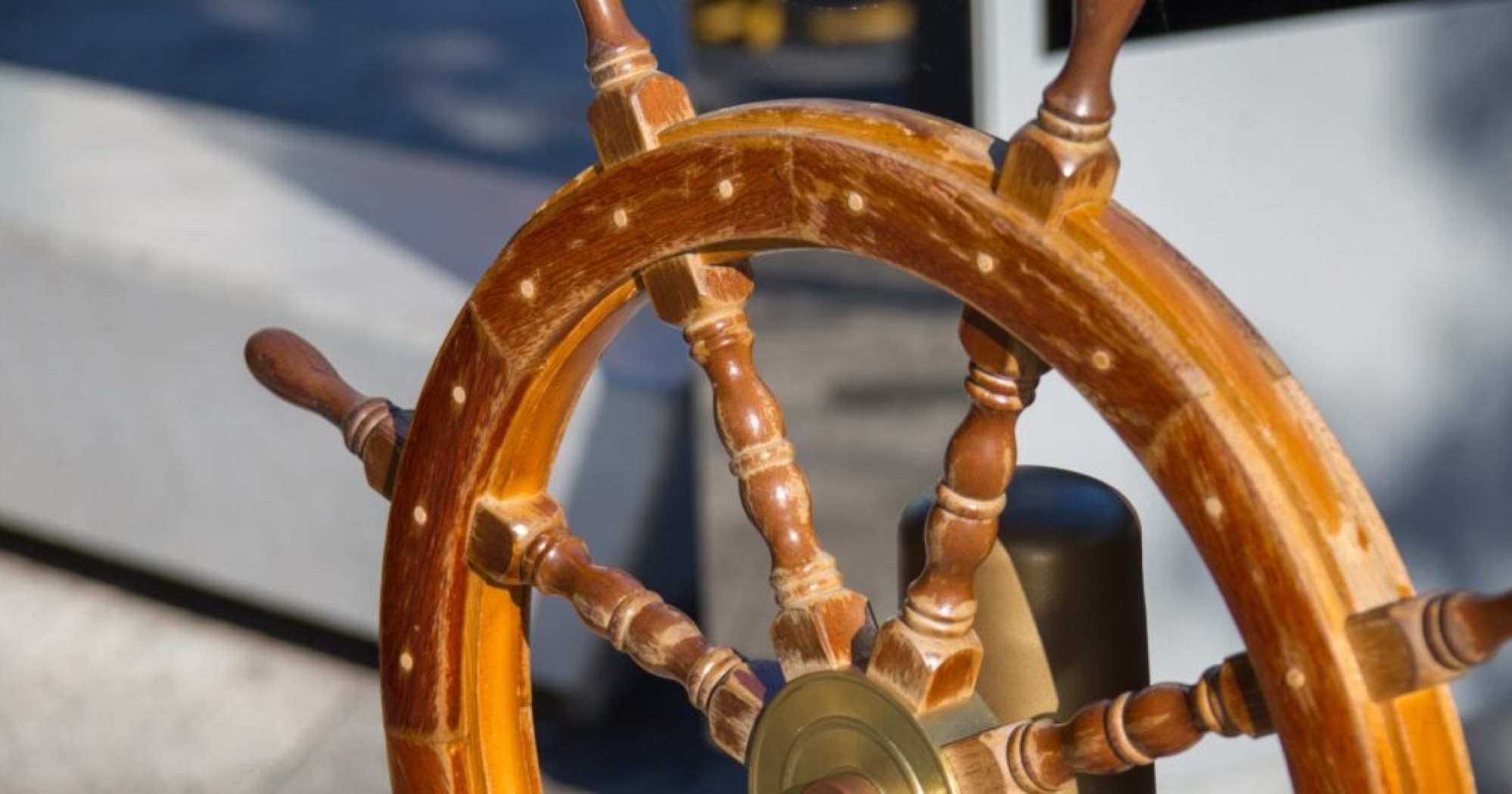 Wooden ship's wheel with brass center, mounted on a boat deck.